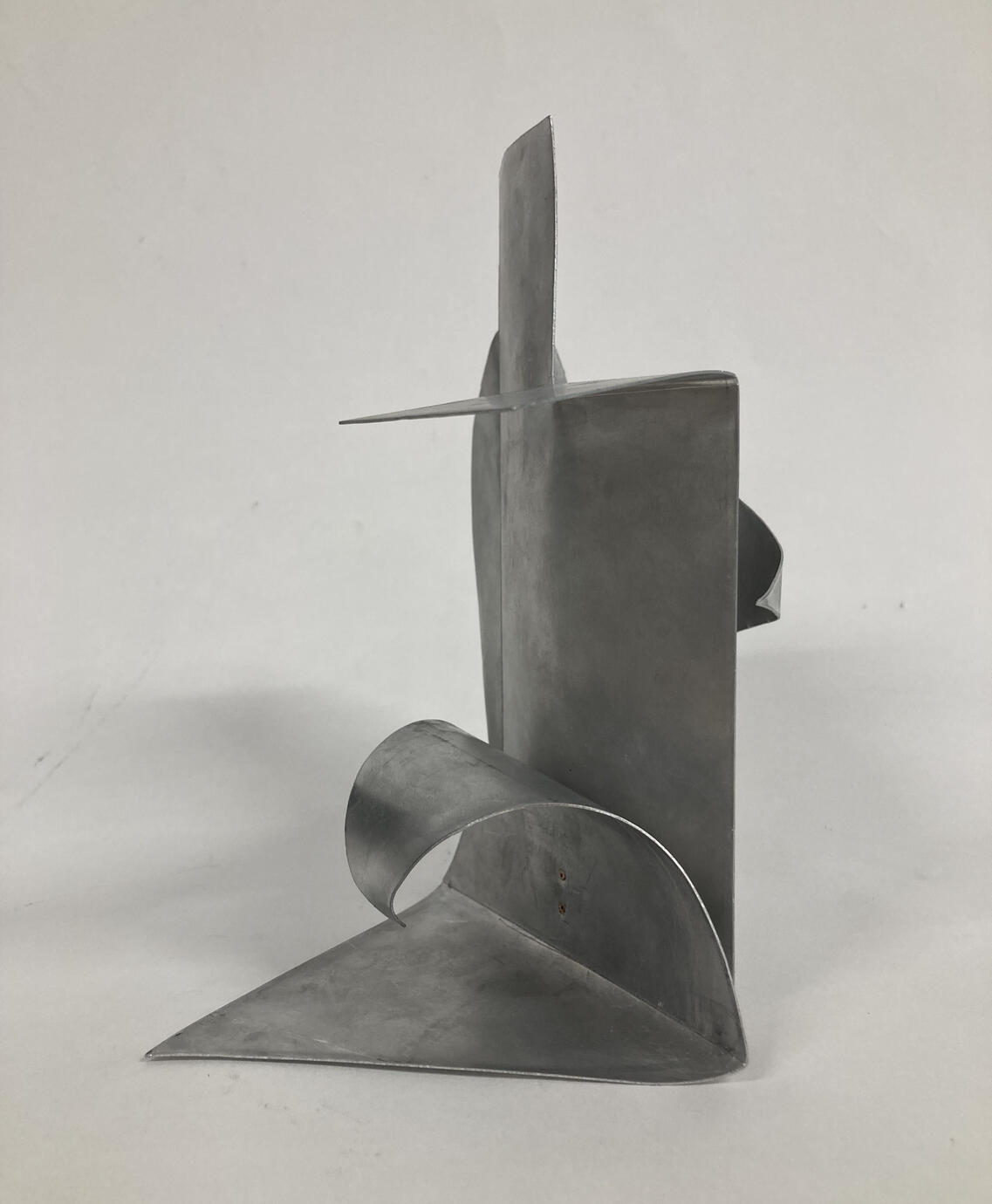 An aluminium sculpture with a main vertical part in the centre, and second part curved to make a wave shape, attached to the centre part with a copper rivet.