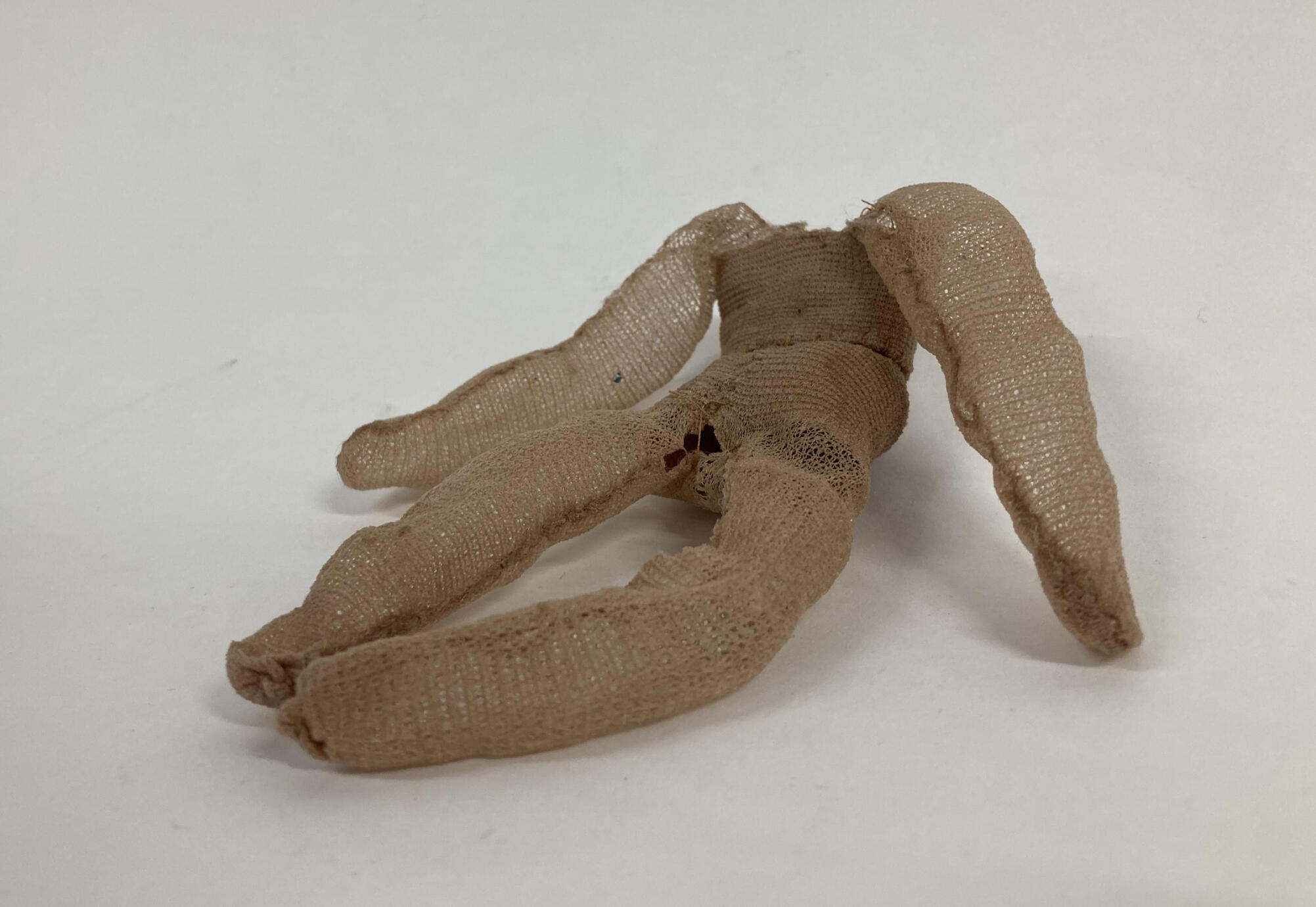A headless, human shaped figure made from tan nylon tights material, held solid with clear glue, in a sitting position with outstretched legs.