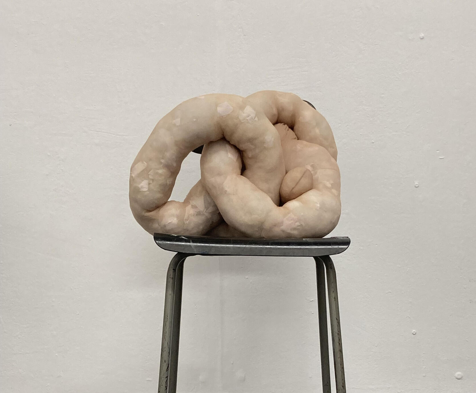 A light tan pair of tights stuffed with white material and twisted into a knotted shape, placed on a black stool.