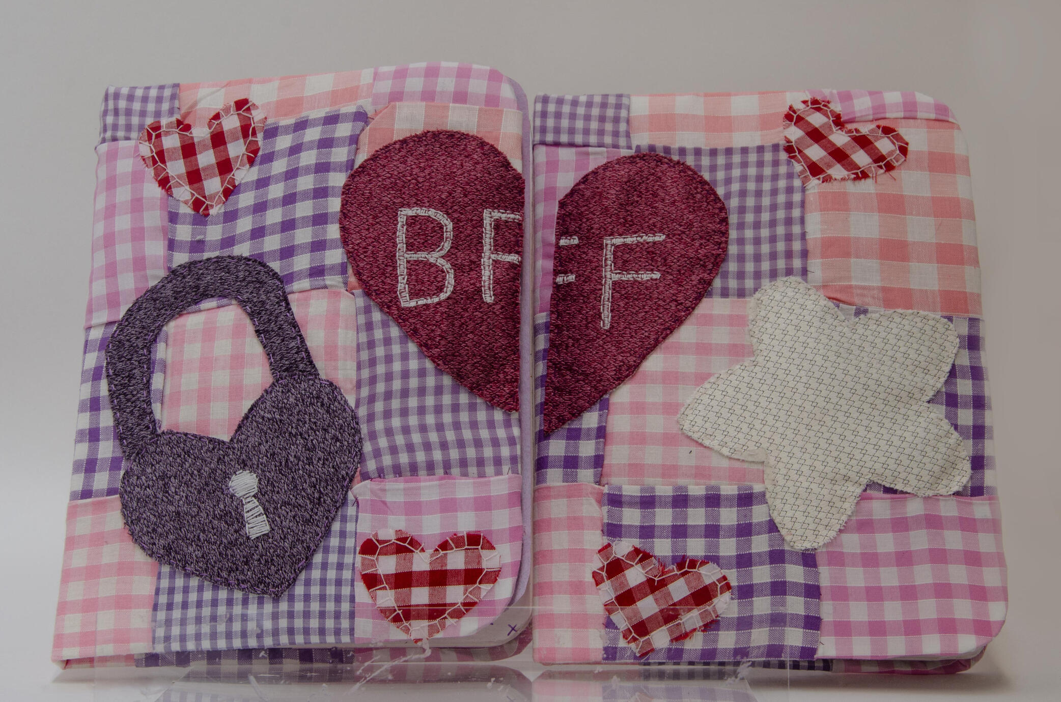 Two diaries with pink and purple quilted gingham covers, with applique hearts, stars and padlocks, with half a heart on each one that come together to spell 'BFF' across the two diaries.